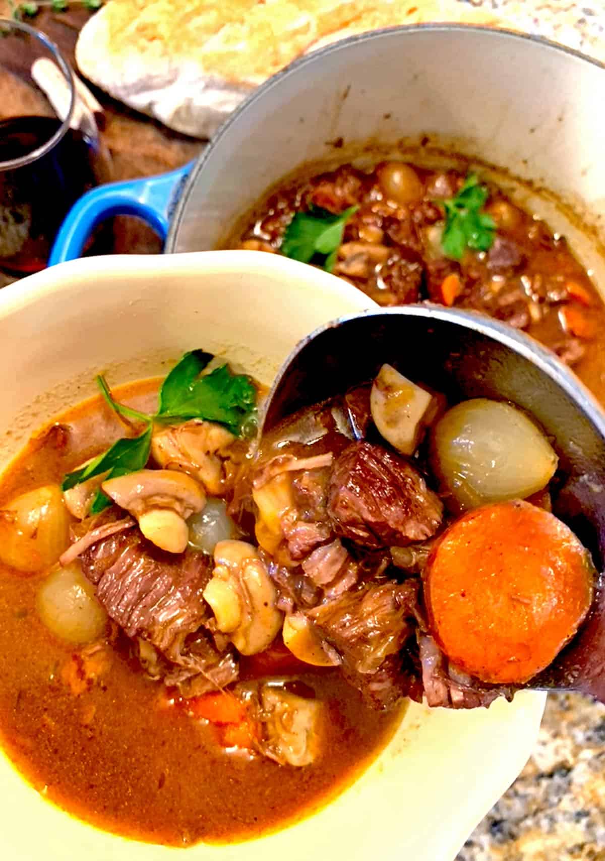 A ladle of beef stew being served in a bowl.