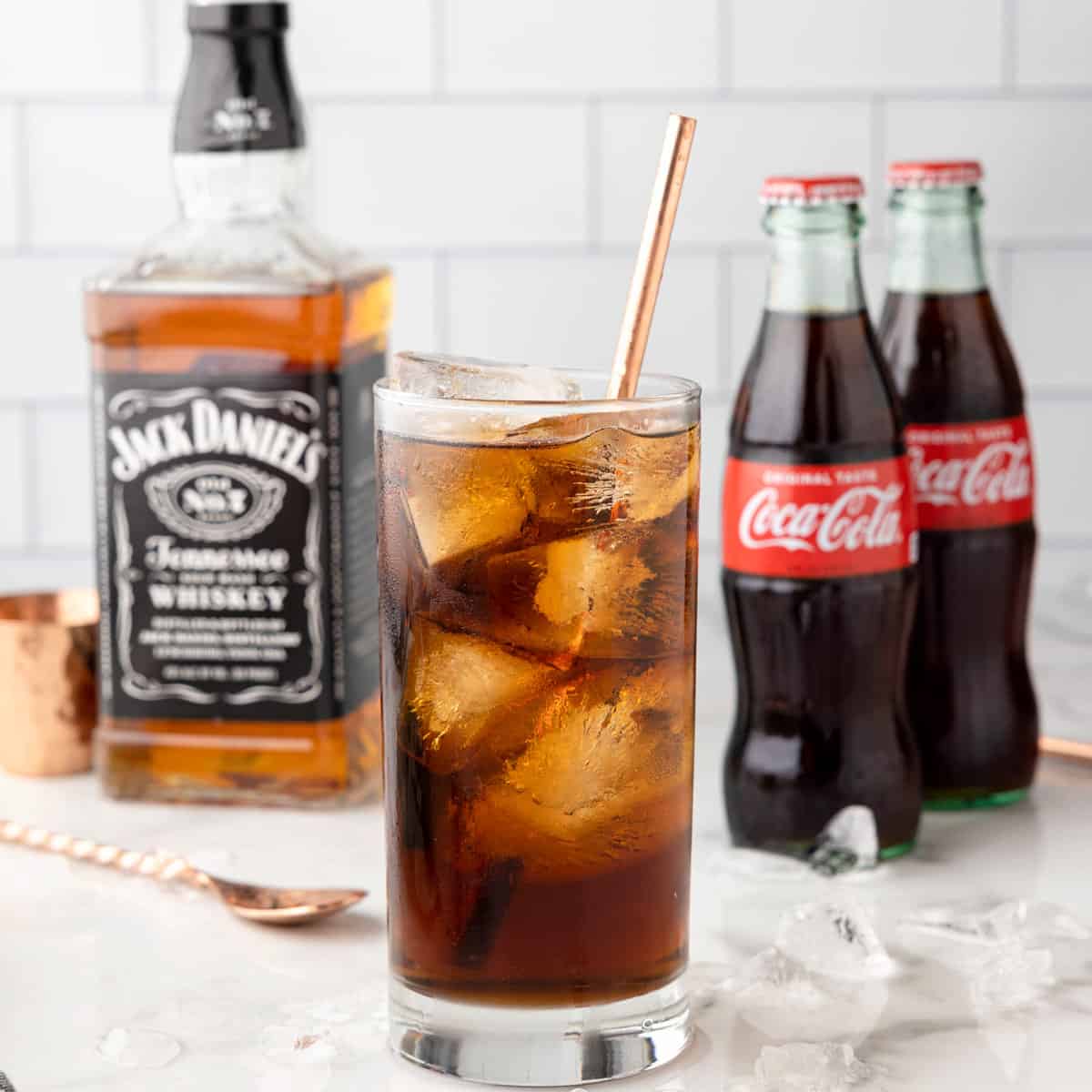 A jack and coke with bottle of Jack Daniels and 2 coke bottles.