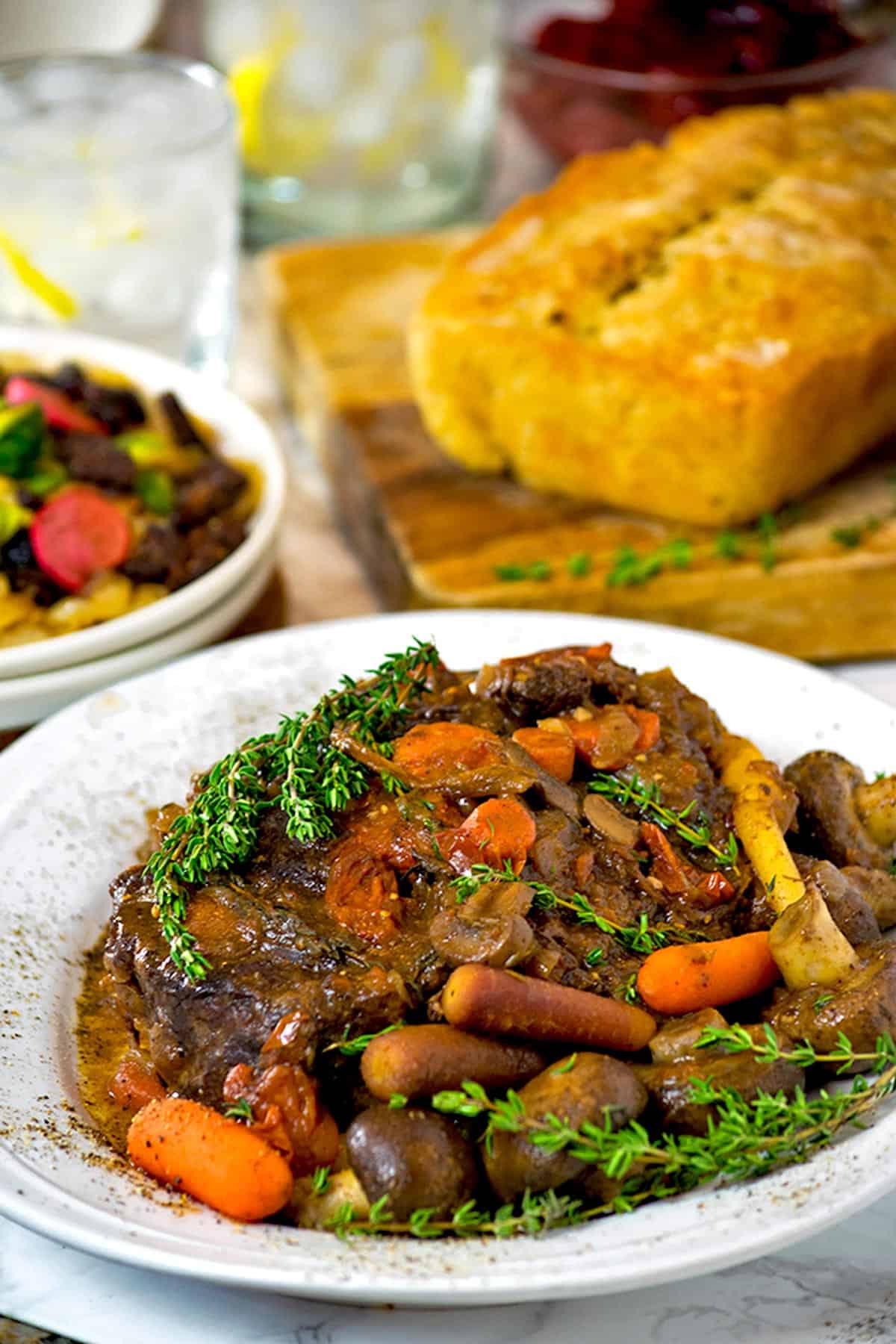 A plate of braised beef with fresh thyme and vegetables.