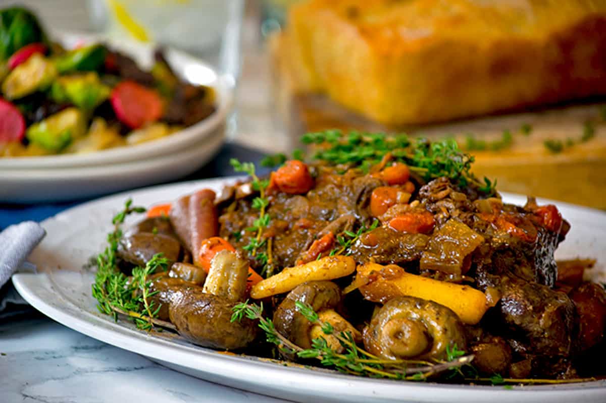 A plate of braised beef with vegetables and fresh thyme sprigs.