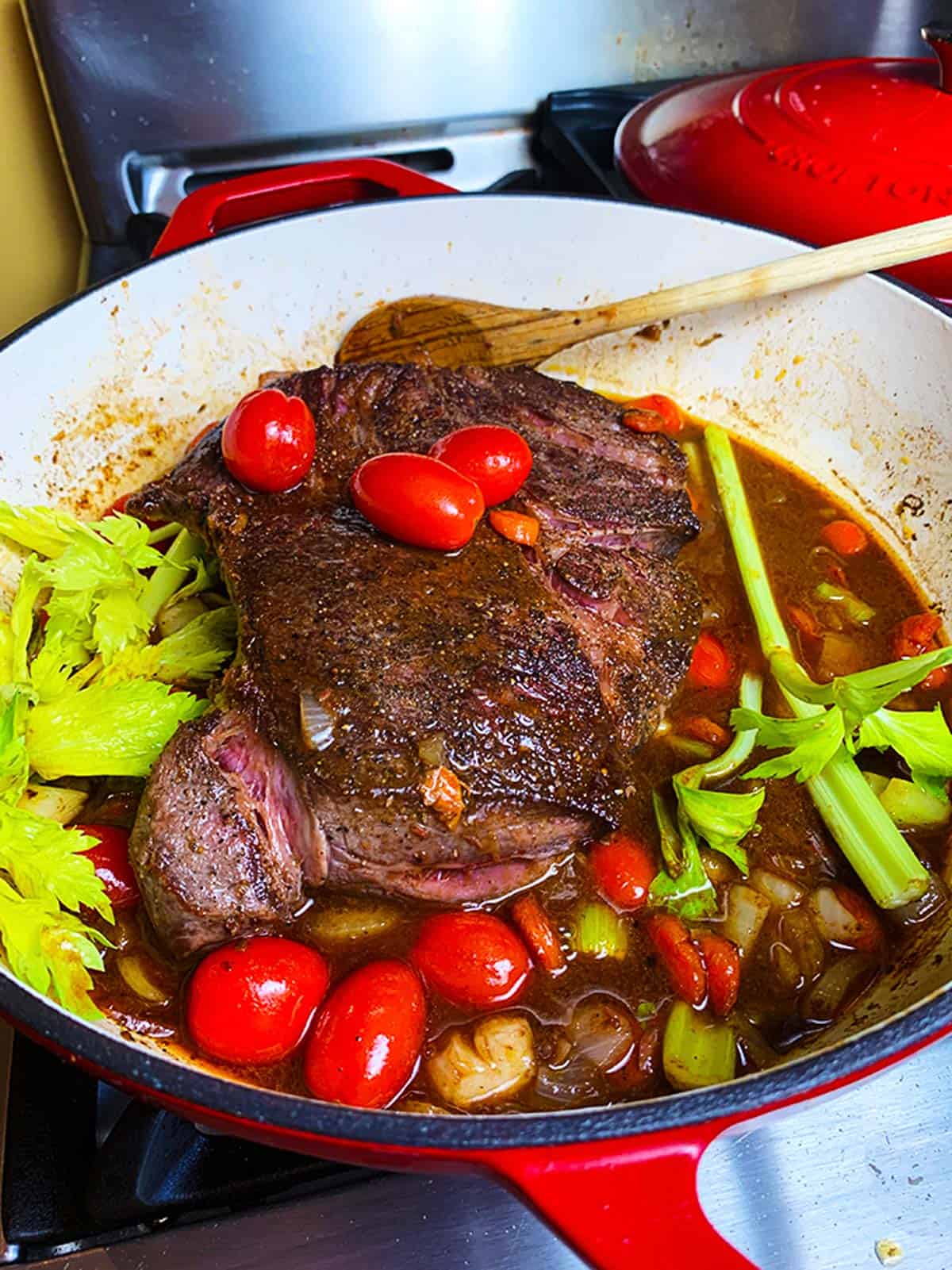 A chunk of beef in a large skillet with sauce and vegetables.
