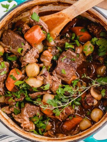 A pot of beef bourguignon with a wooden spoon.