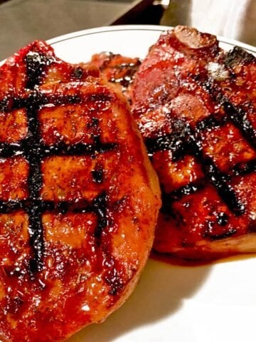 Two seared pork chops on white plate.