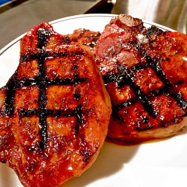 Two seared pork chops on white plate.