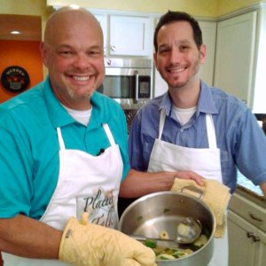 Two chefs in a kitchen, holding a pot.