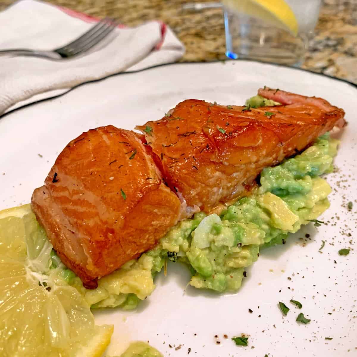 A piece of smoked salmon on a bed of guacamole.