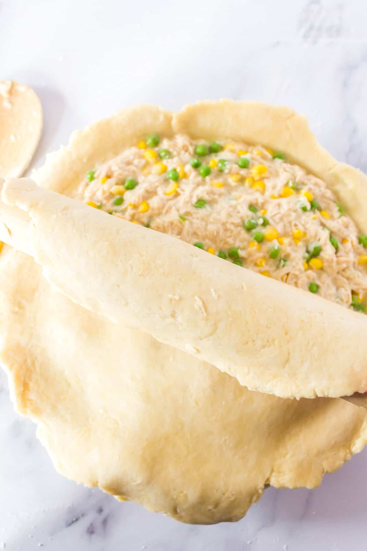 Placing the top layer of a pie onto a turkey pot pie.