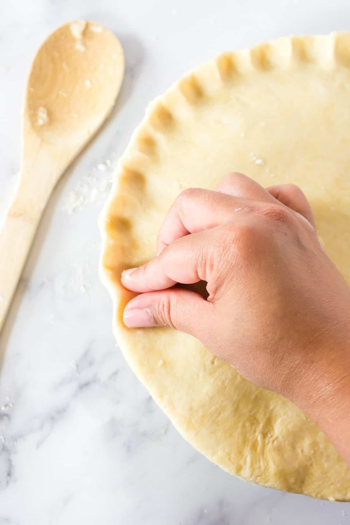 Someone's hand and fingers crimping a homemade pie crust.