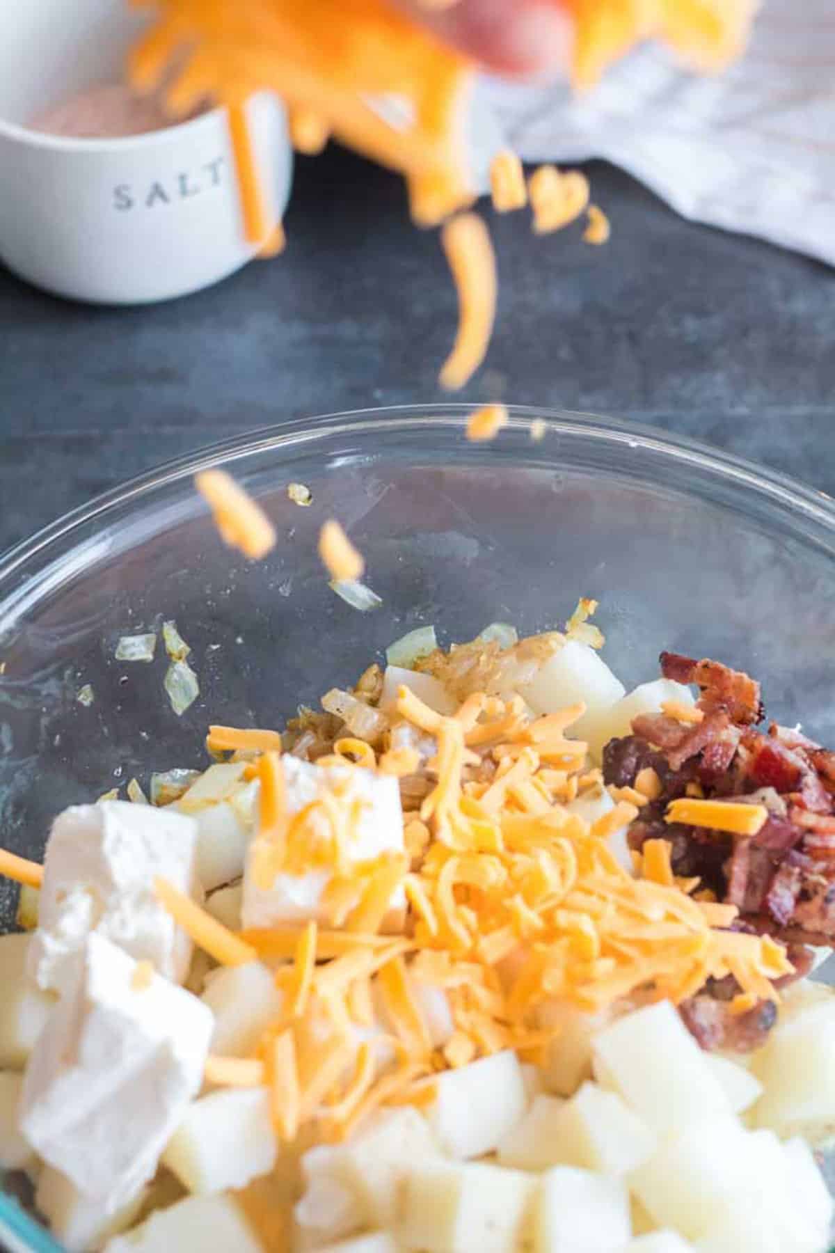 Adding shredded cheese to a mixing bowl with other ingredients.