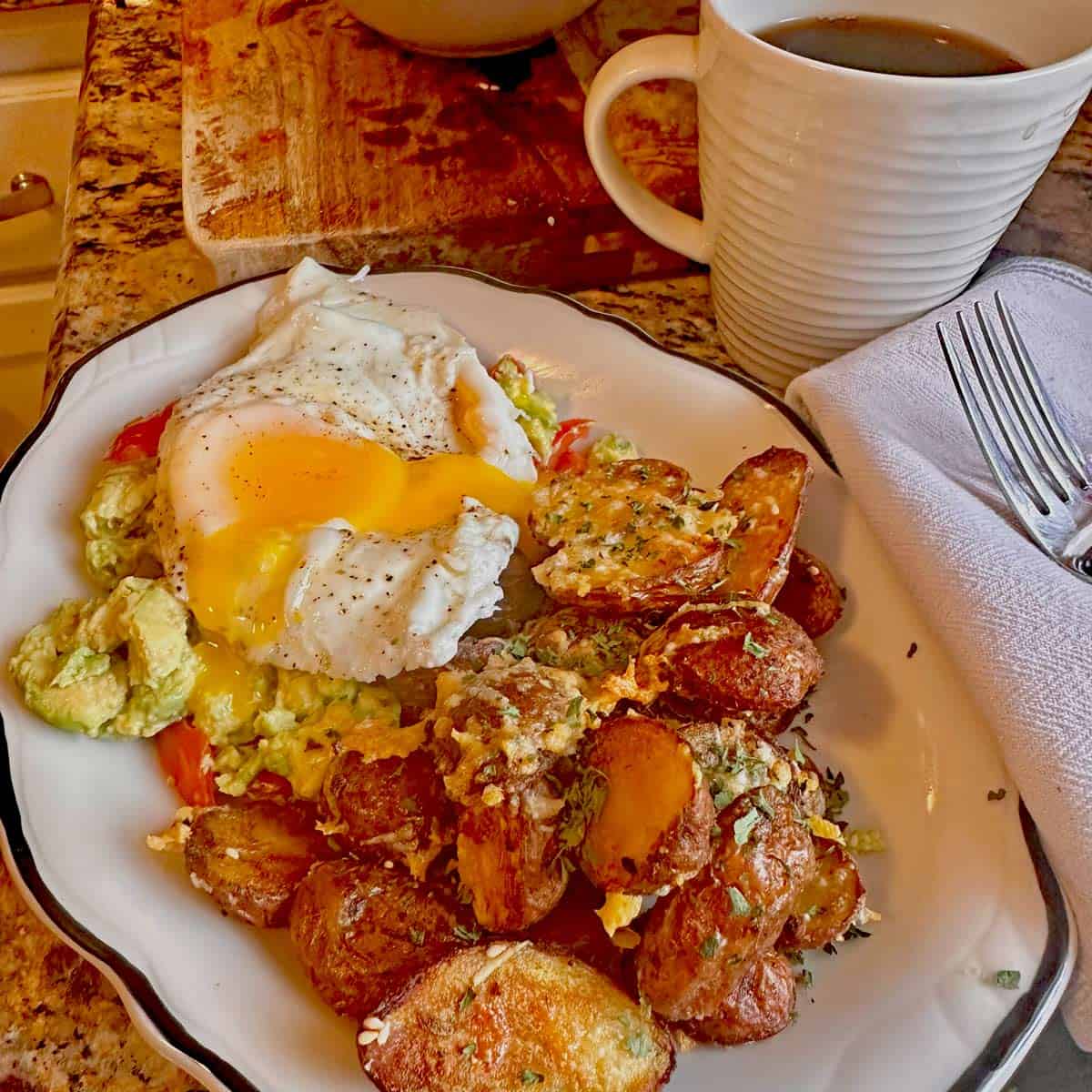 A plate of breakfast potatoes with a fried egg and guacamole.