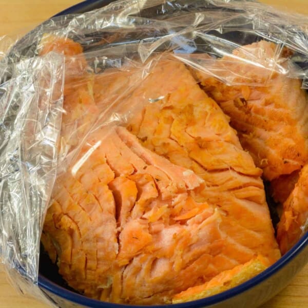 A plate of leftover salmon with plastic wrap.