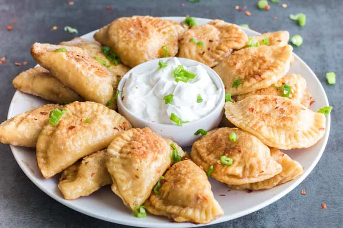 A plate of Polish dumplings with sour cream and chopped chives.