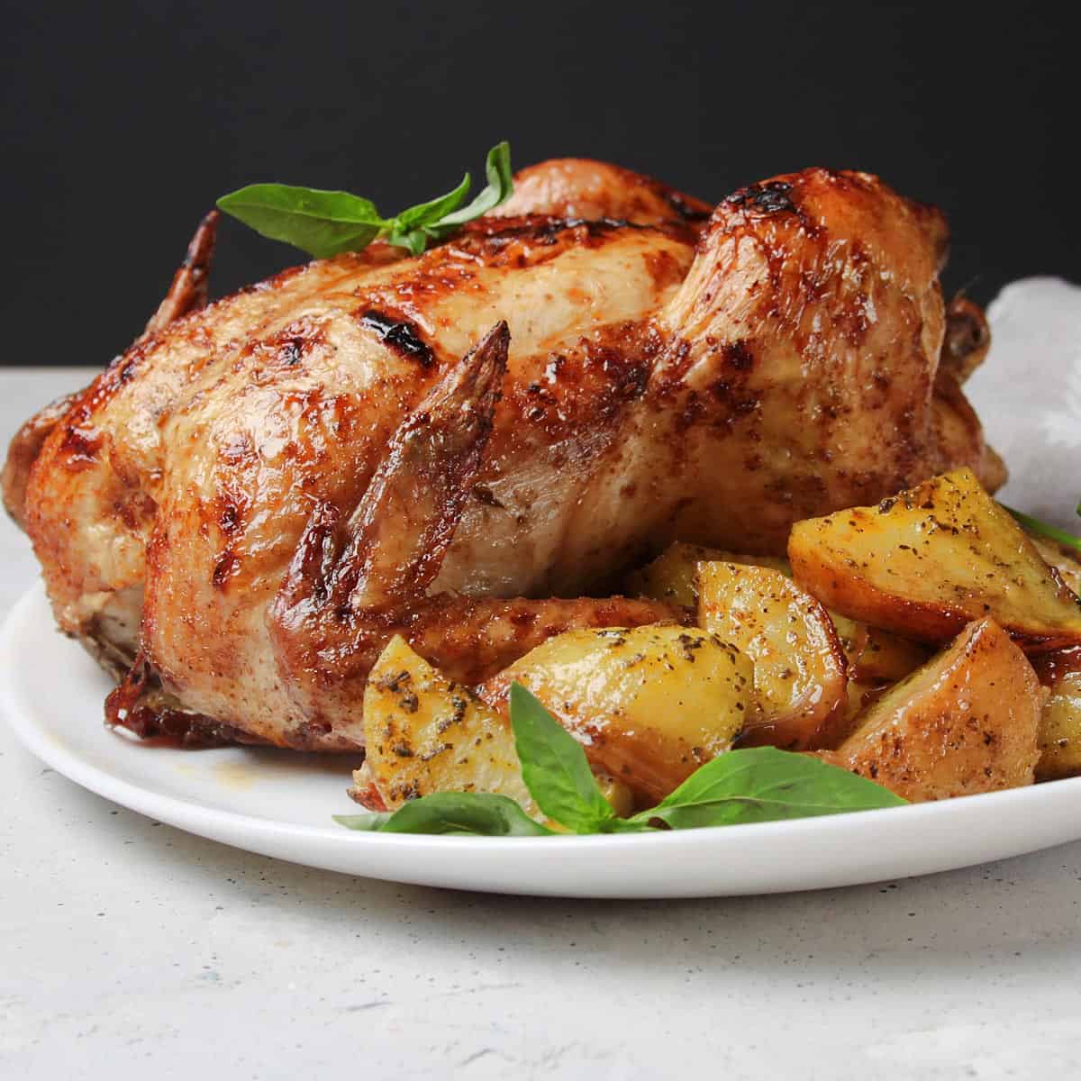 A roasted chicken on a plate with some crispy potatoes.