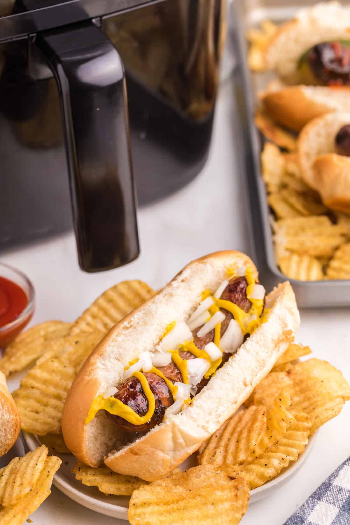 A bratwurst in a bun, loaded with onion and mustard, with potato chips.