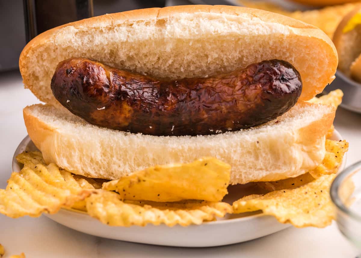 A plain bratwurst on a roll with potato chips.