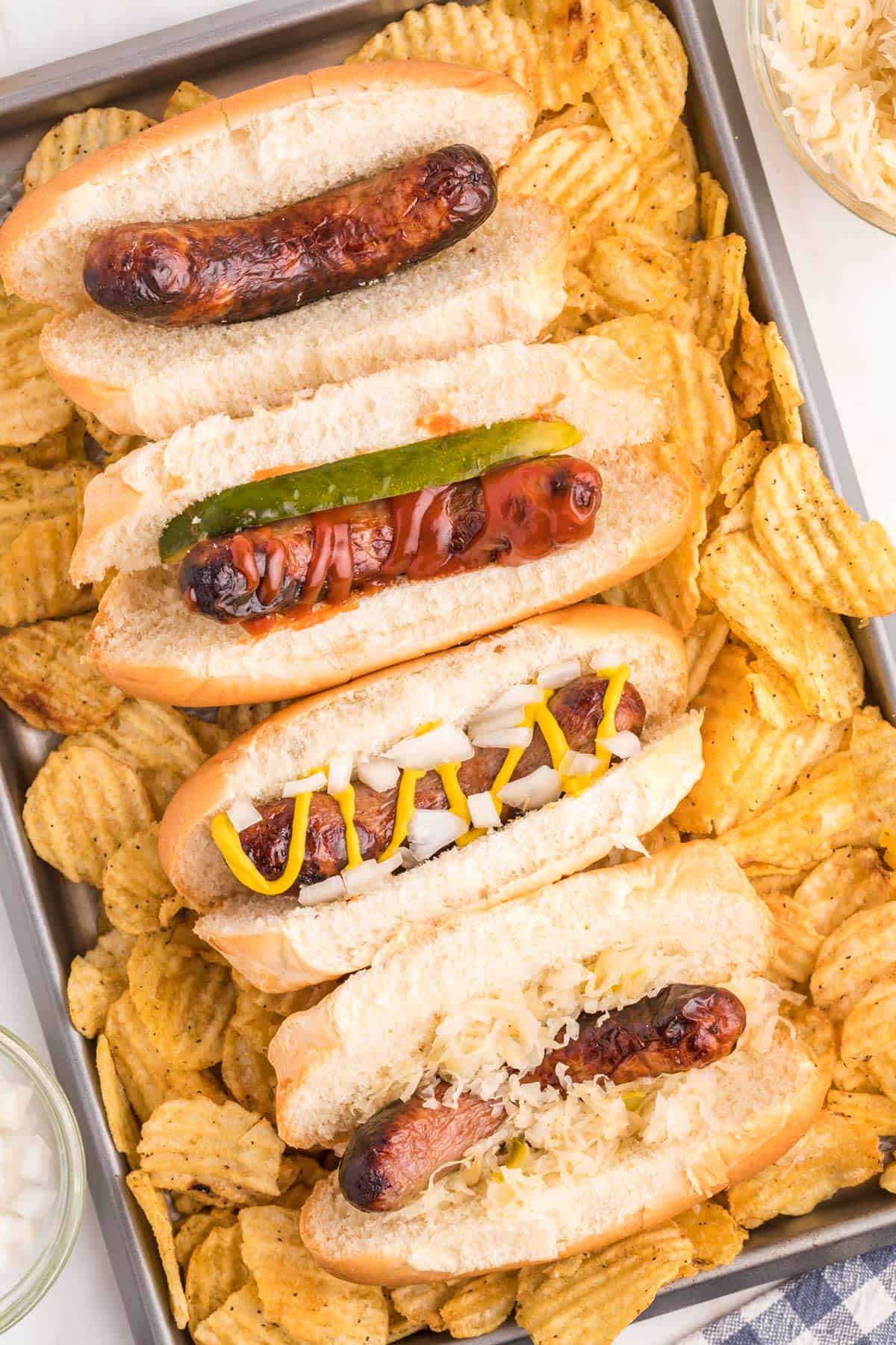 A bunch of brats with different toppings with potato chips.