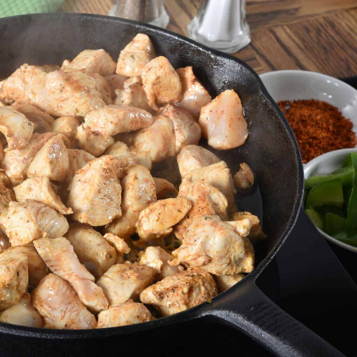 A skillet with diced chicken in it.