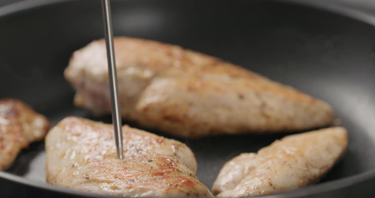 Measuring the temperature of chicken in a pan.