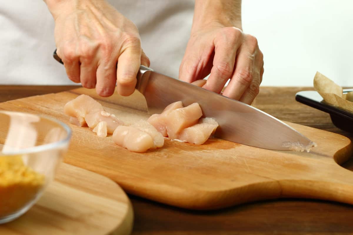Dicing chicken breast on a cutting board.