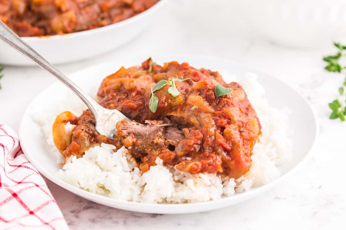 A plate of Swiss steak over a bed of white rice.