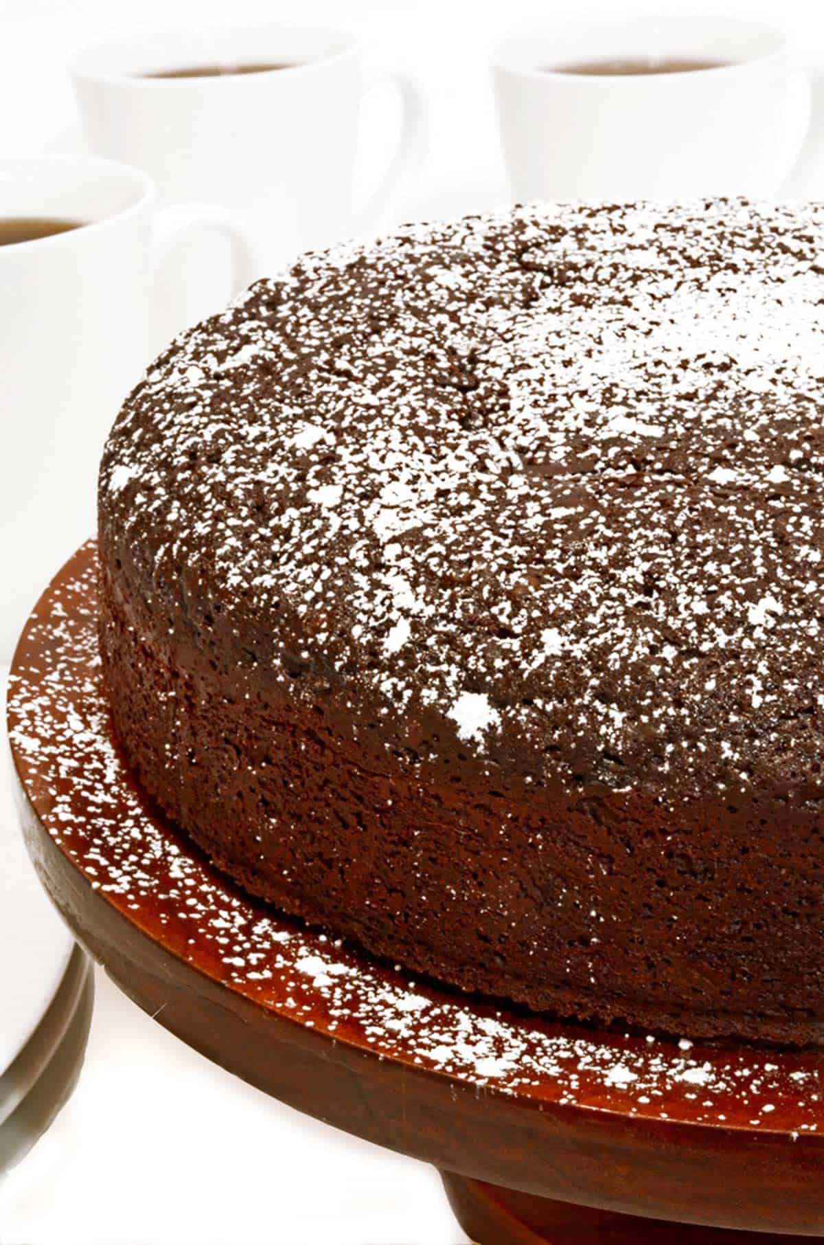 A chocolate cake, dusted with powdered sugar and 3 cups of coffee.