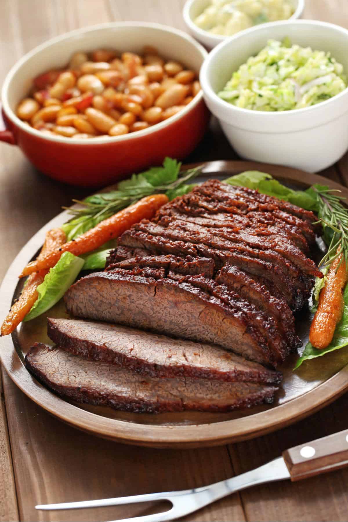 A cut up brisket with some side dishes.