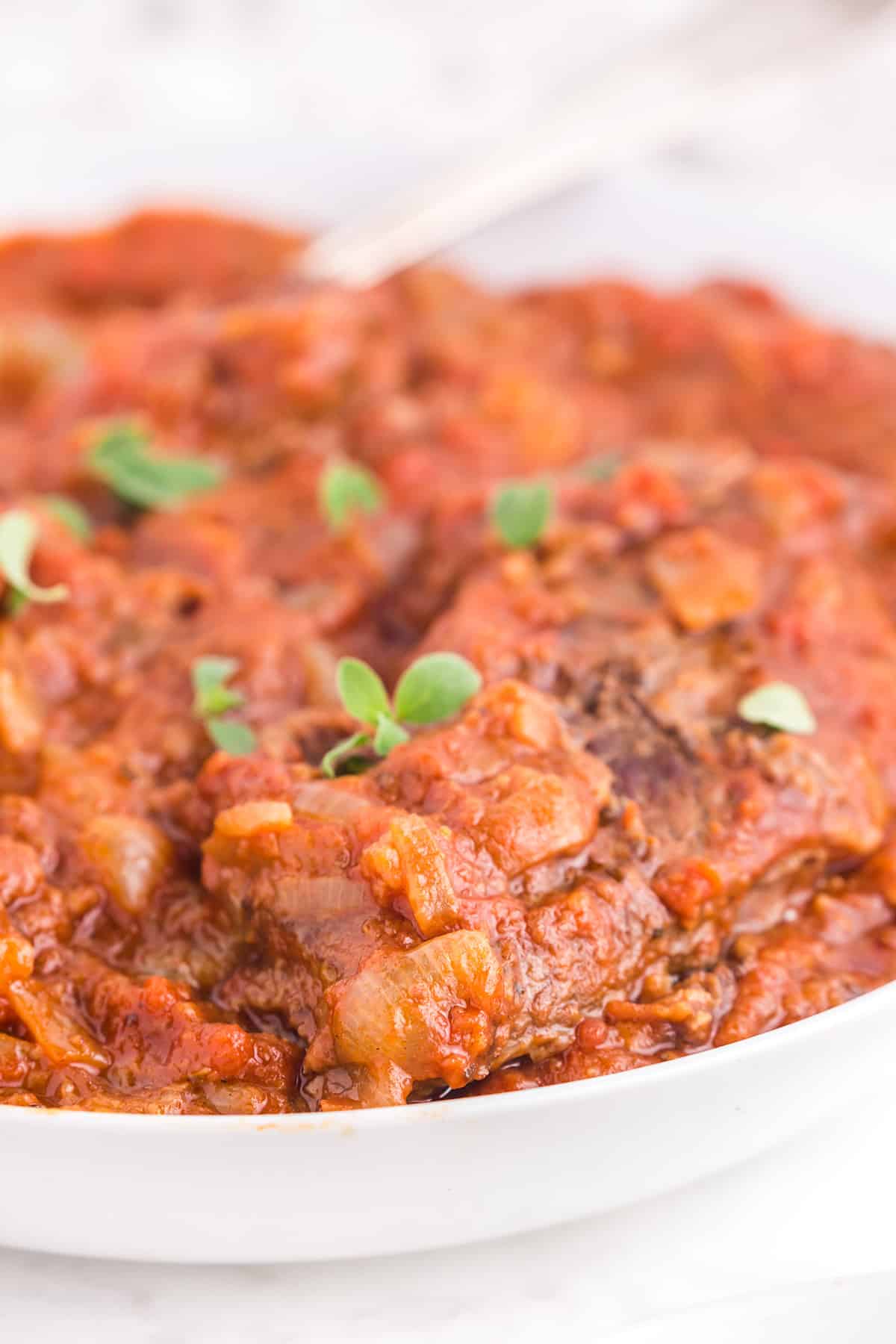 A bowl of Swiss steak with herb garnish.