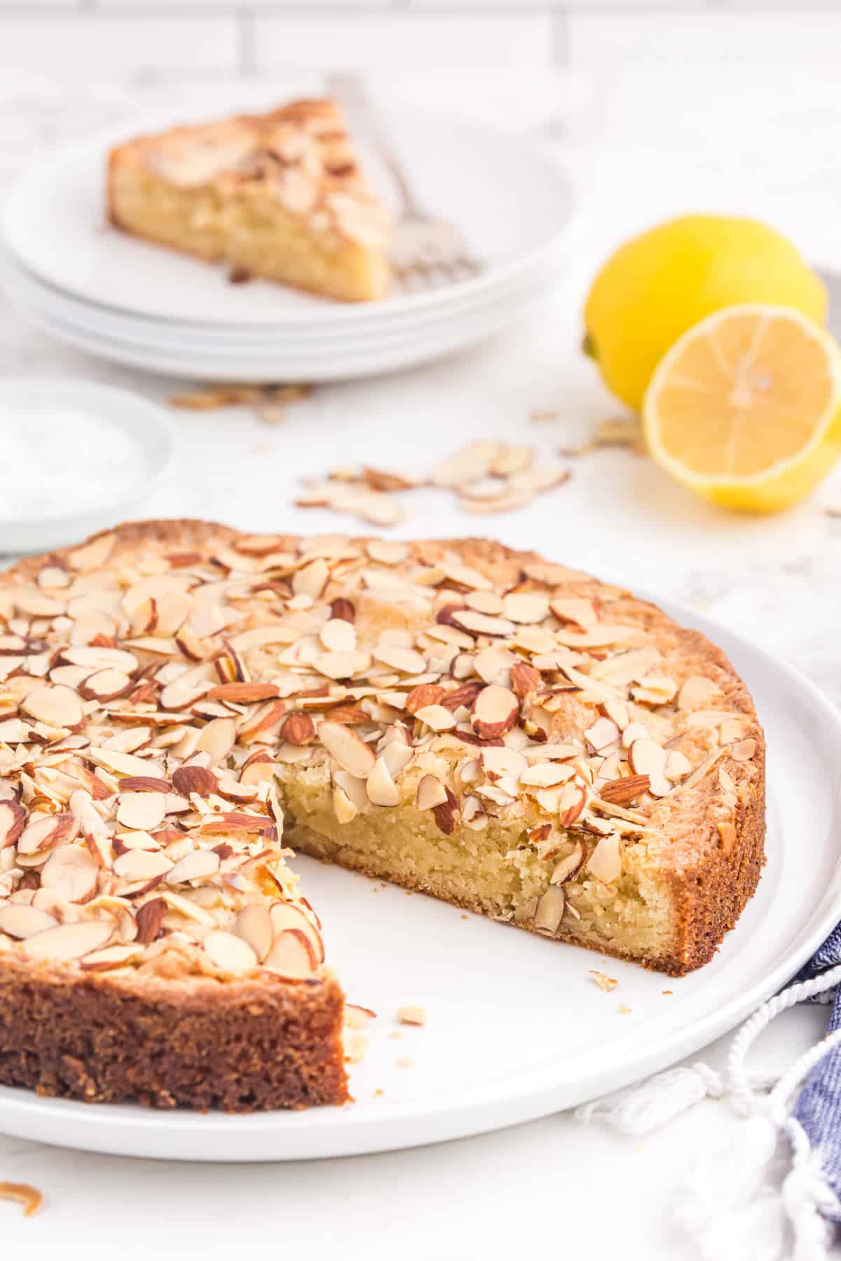 A sliced almond cake with a couple of lemons.