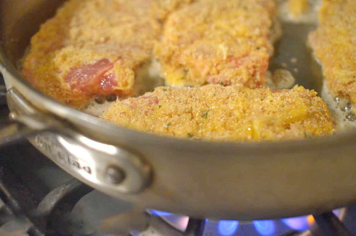 Some breaded pork chops in a skillet.