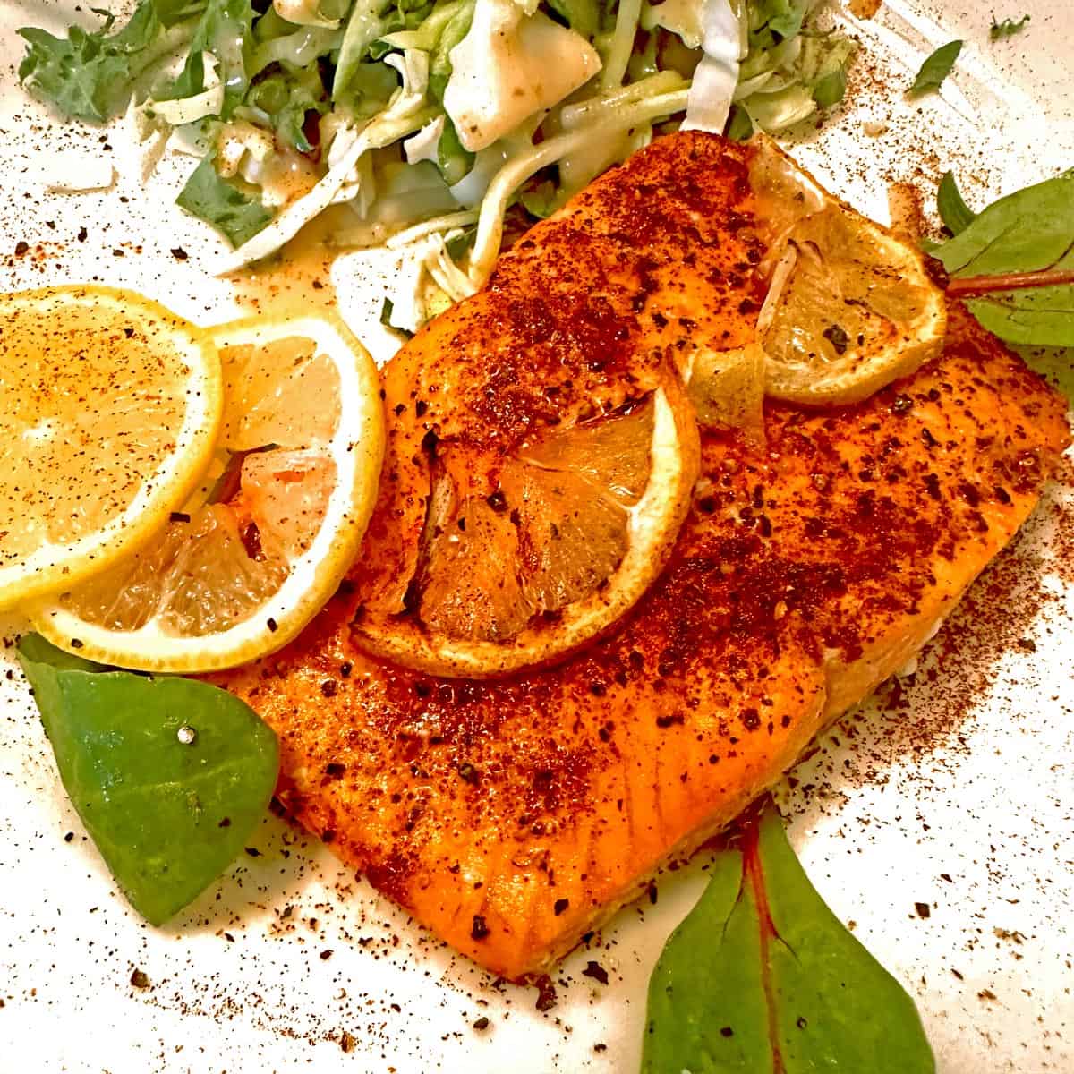 A piece of salmon on a white plate with lemon garnish.