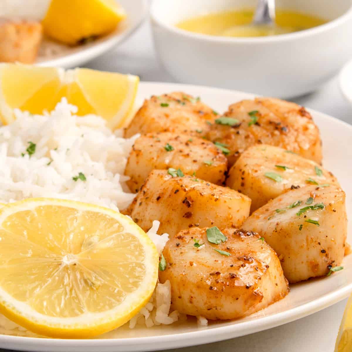 A plate of scallops and rice with lemon wedges.