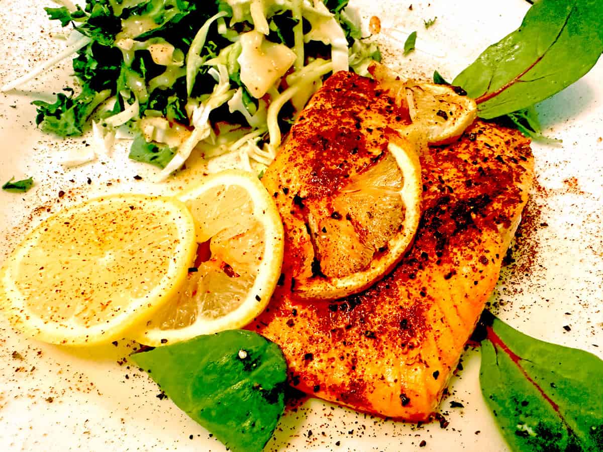 A plate of salmon, greens and lemon garnish.