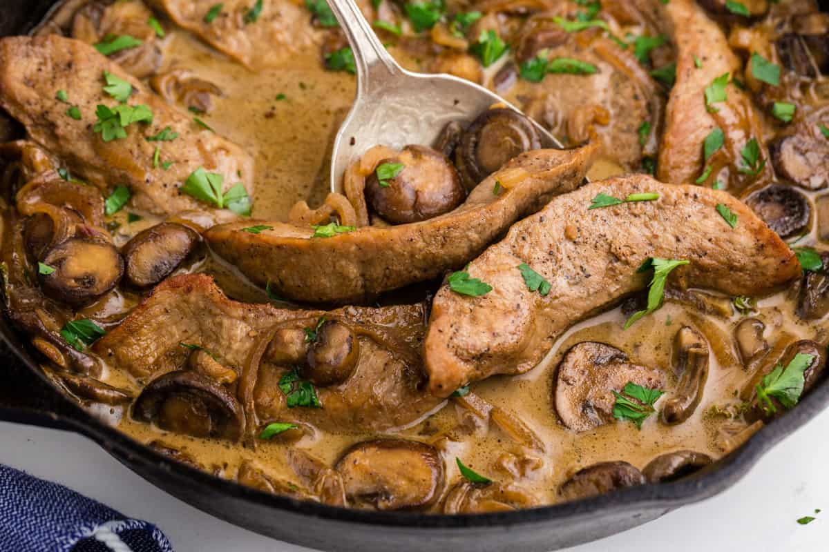A spoon in a skillet of veal Marsala.
