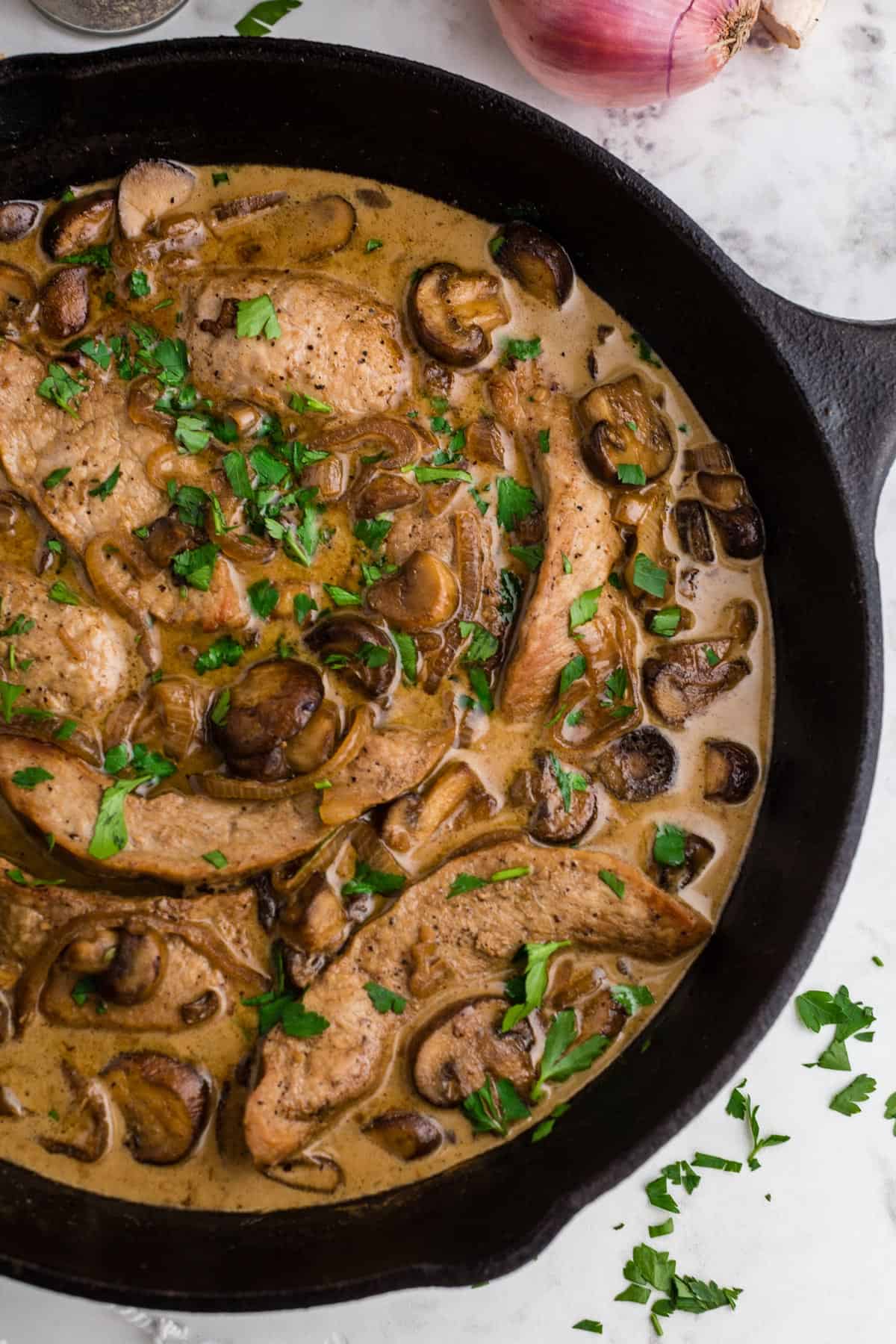 A skillet of veal Marsala topped with chopped parsley as a garnish.