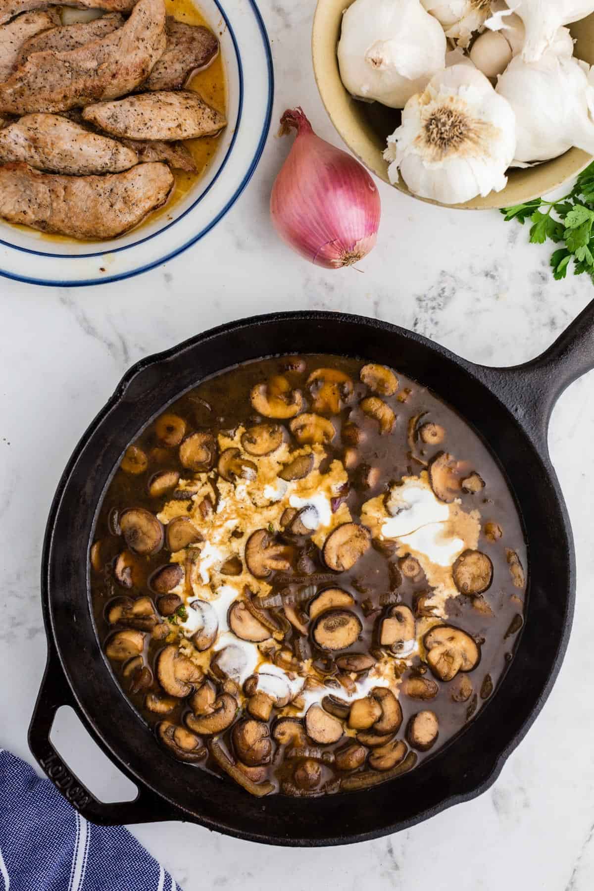 A skillet of mushrooms and broth with a swirl of cream.