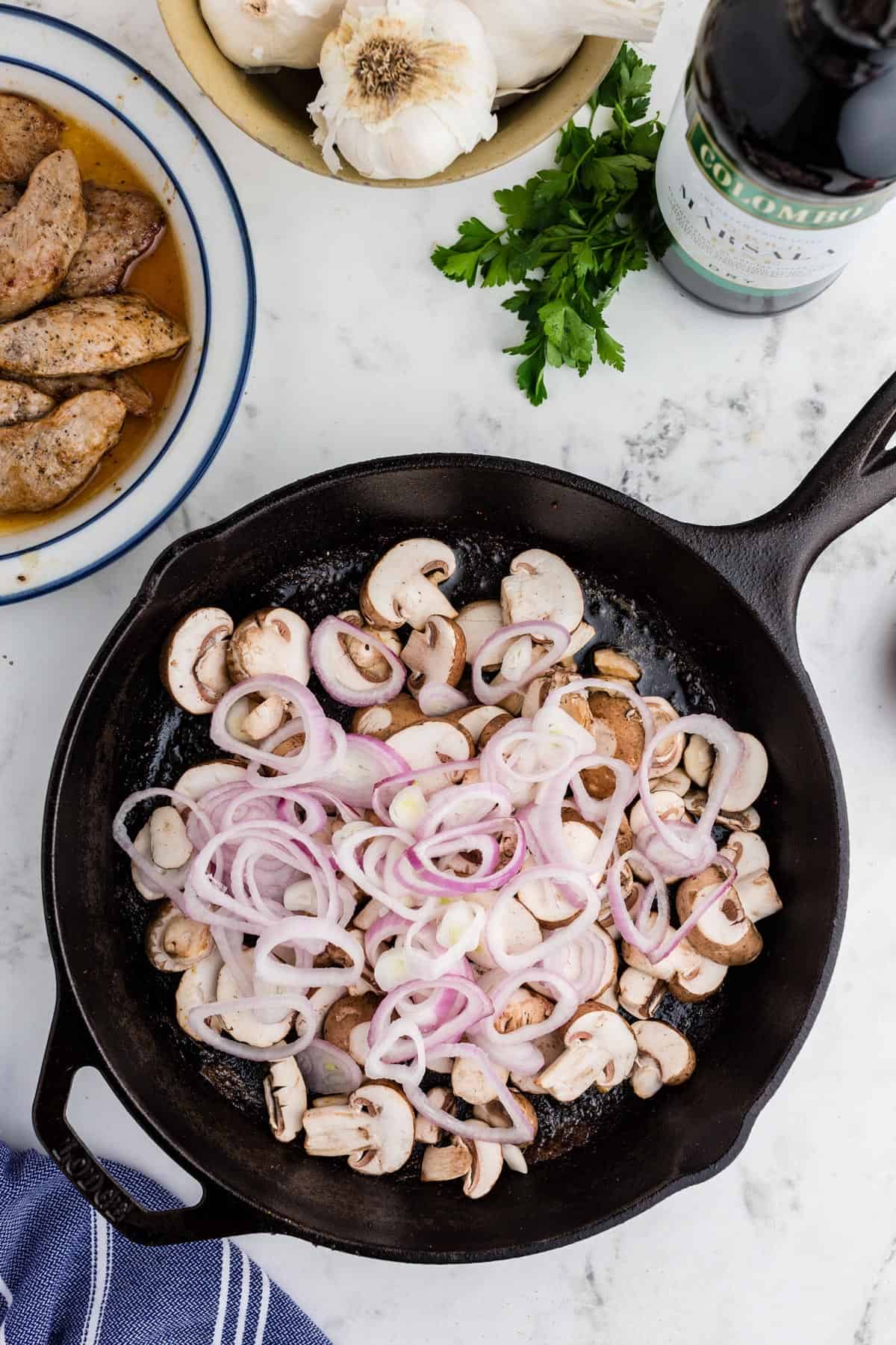 A skillet of uncooked mushrooms and scallions.