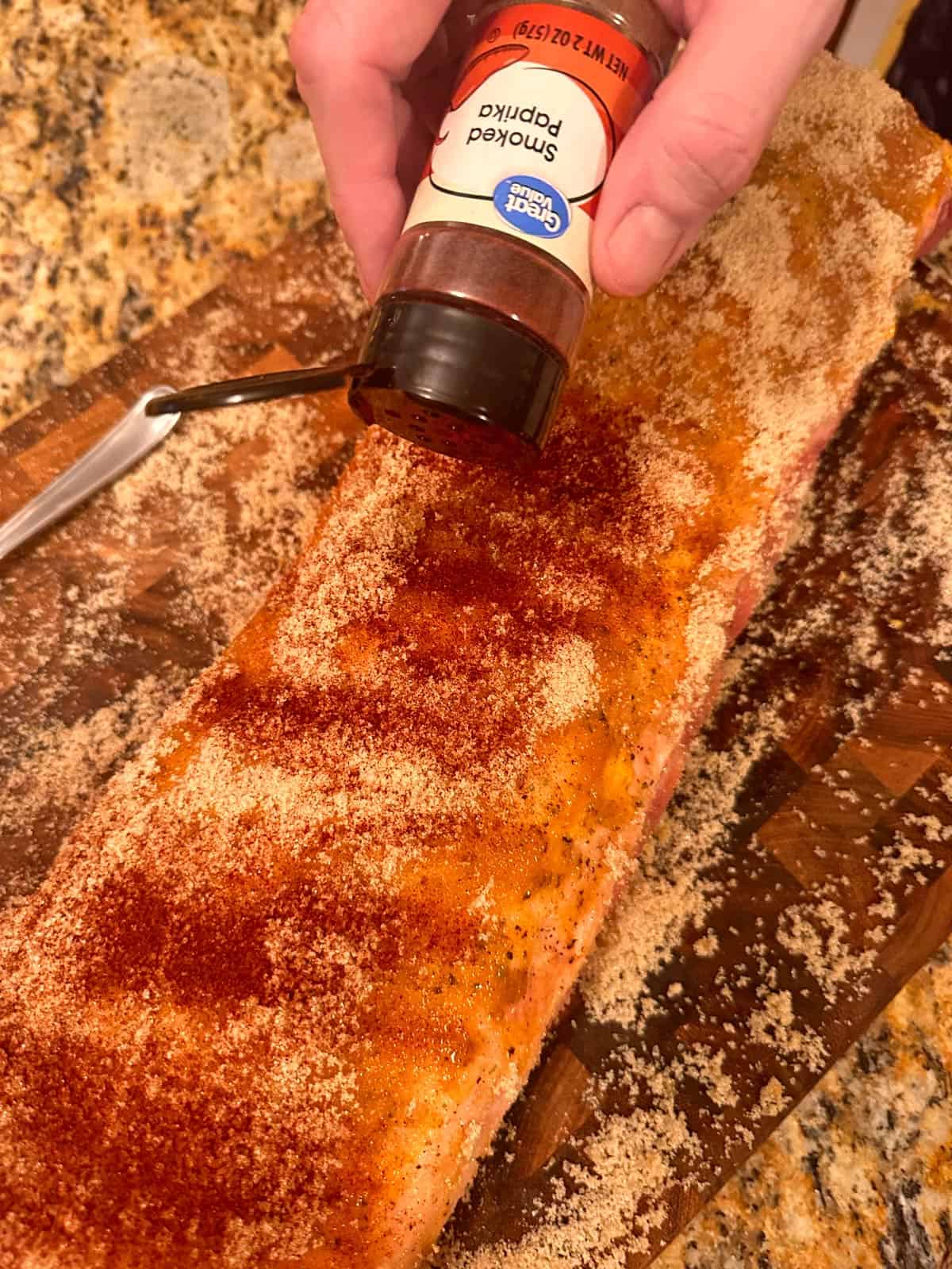 Sprinkling paprika on a long piece of meat.