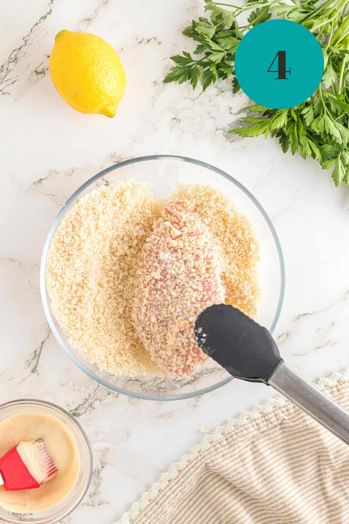 Dipping a piece of raw chicken into a panko mixture.