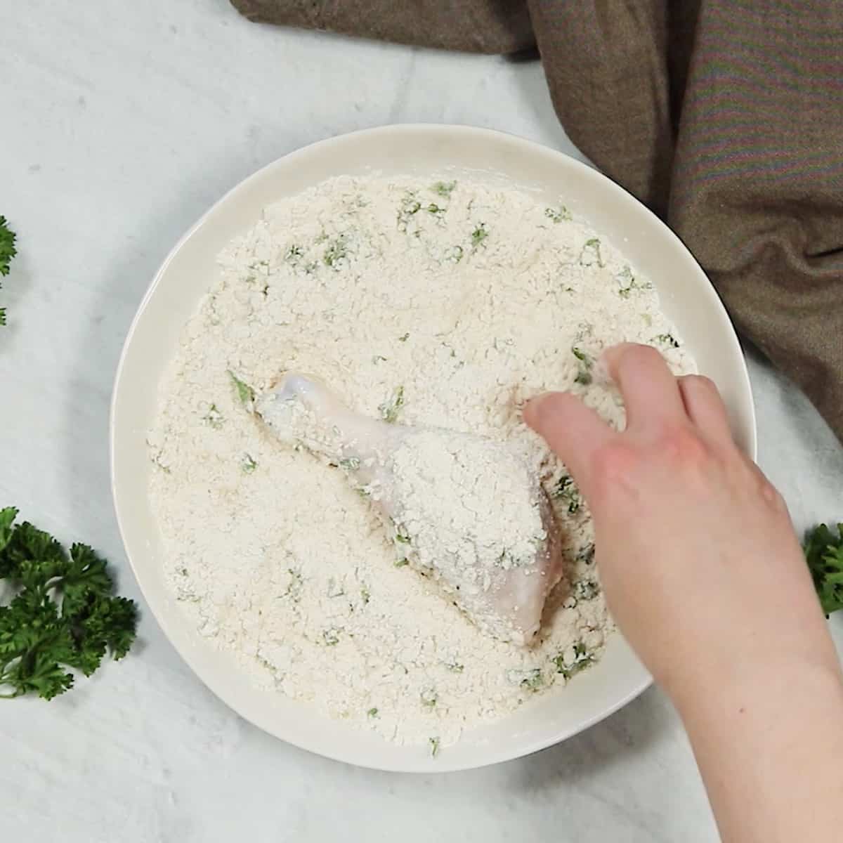 Dredging chicken in a bowl of flour.