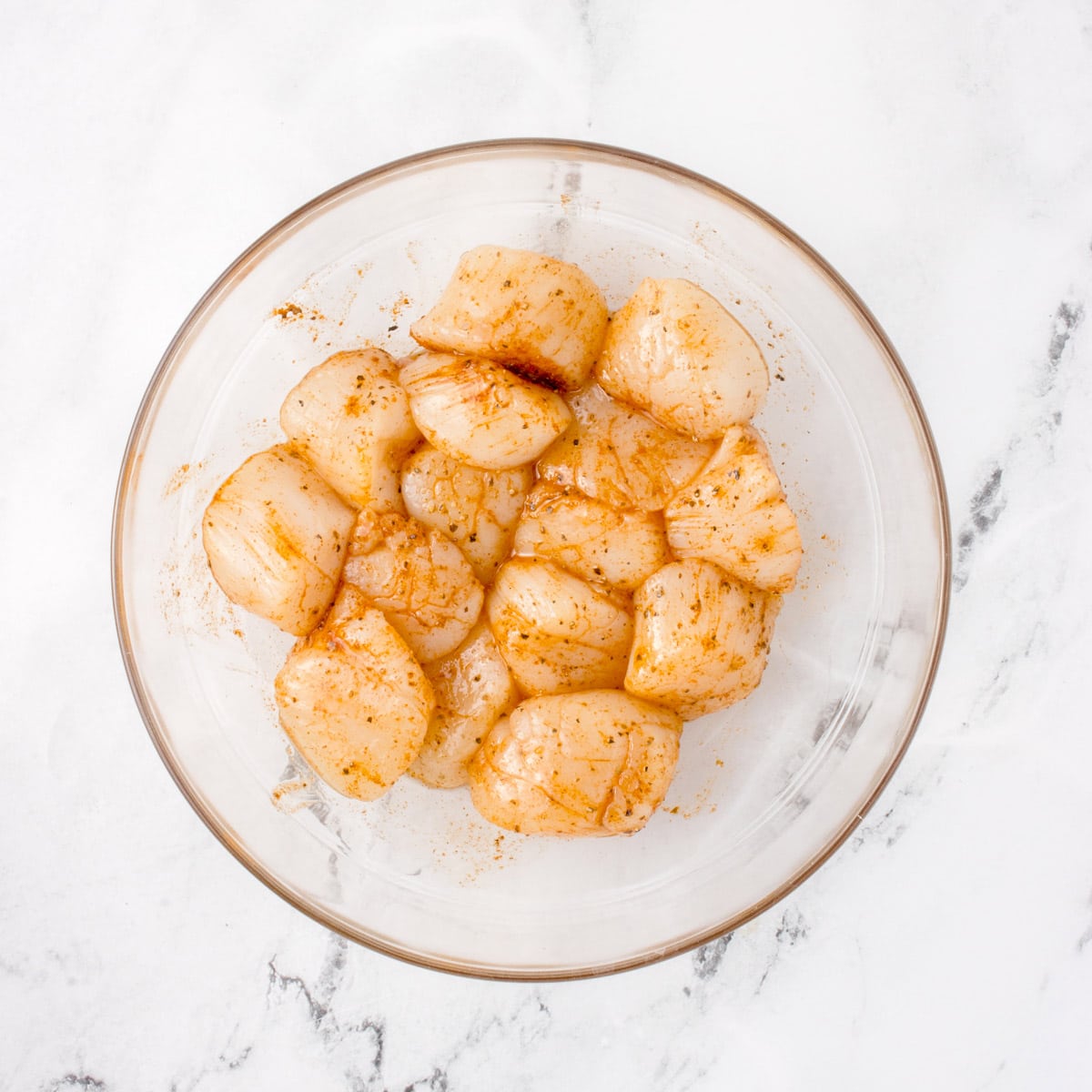 Some seasoned raw scallops in a bowl mixing bowl.