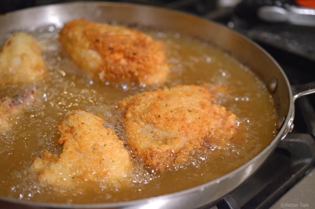 A skillet with chicken frying in oil.