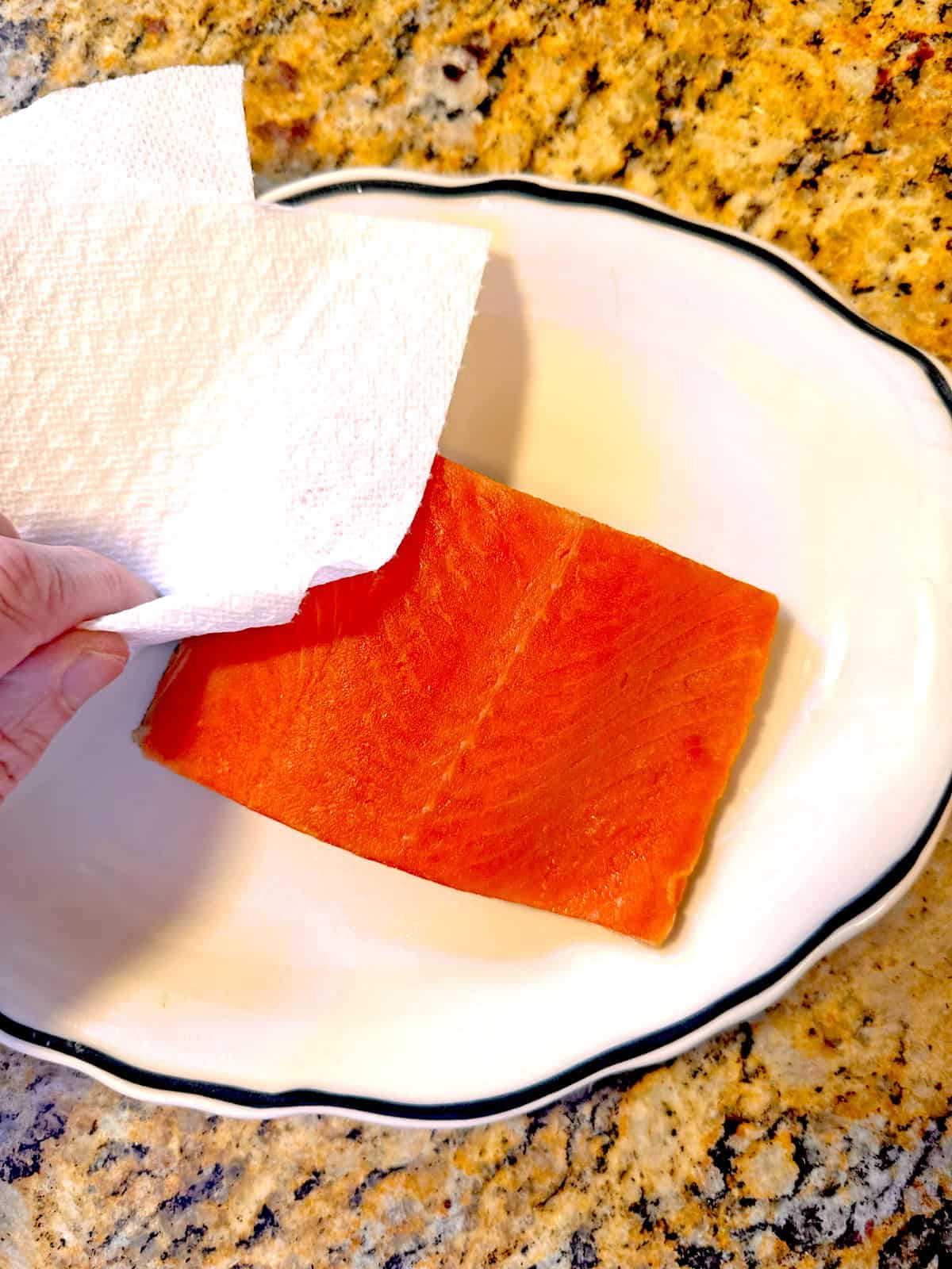 Patting a piece of salmon dry with a paper towel.