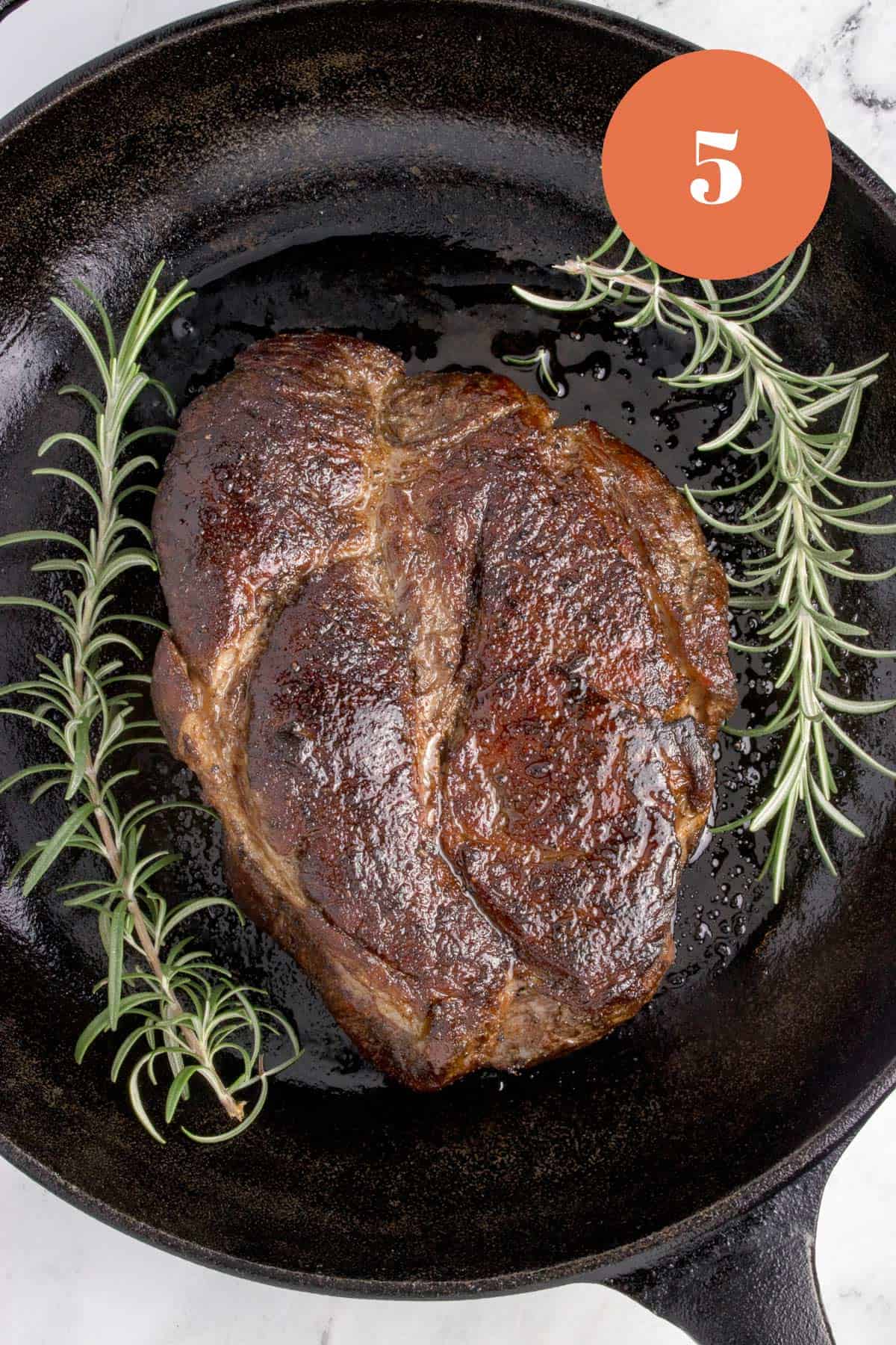A chuck roast with rosemary springs being seared in a cast iron skillet.