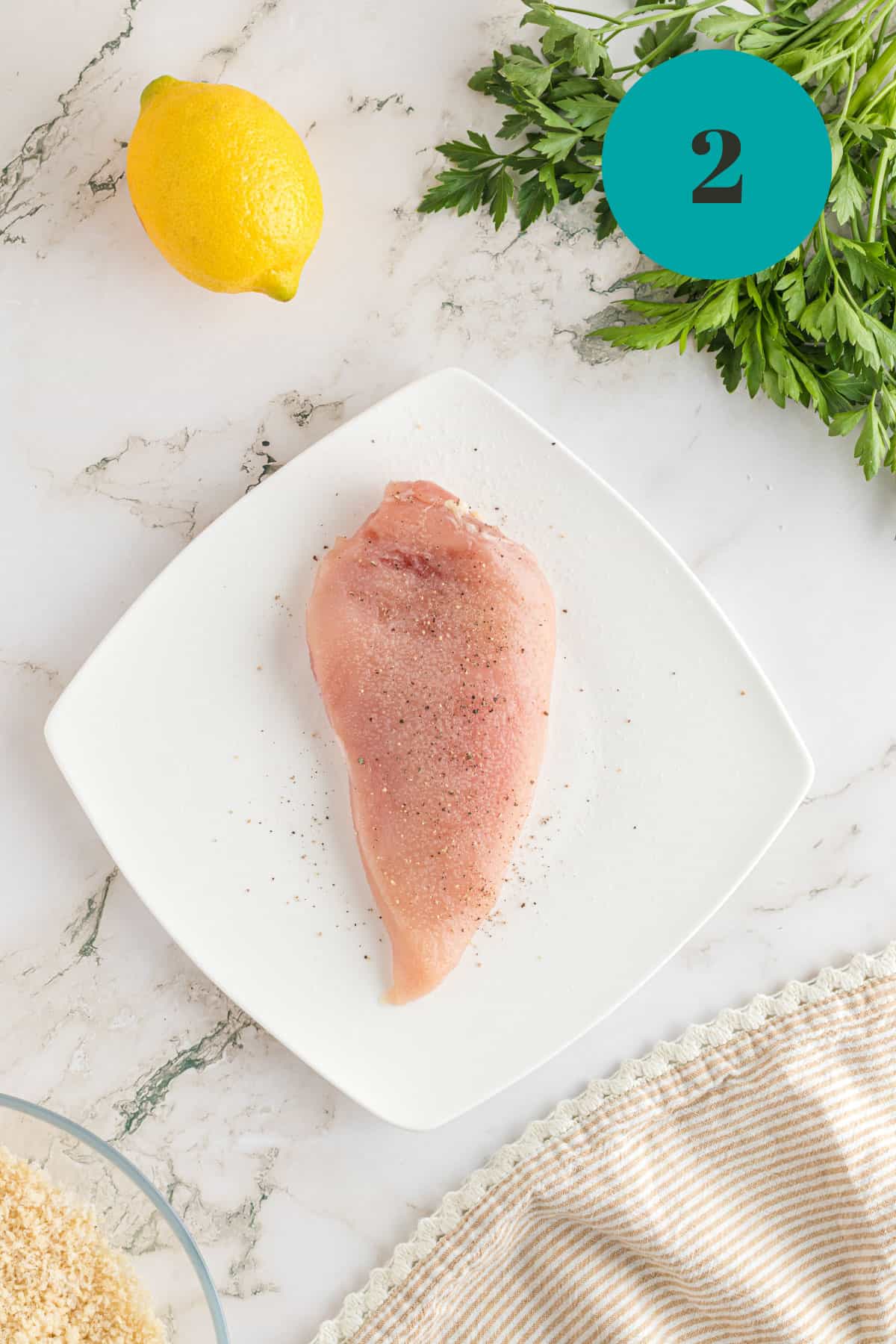Adding salt and pepper to a piece of raw chicken.
