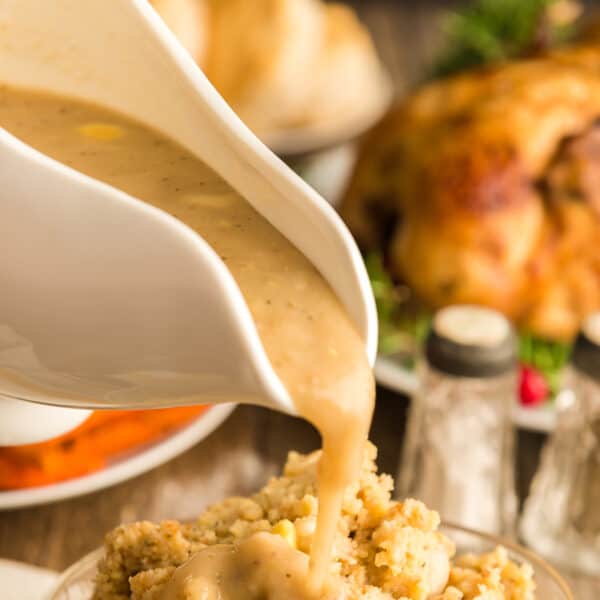 A gravy boat full of gravy being poured on stuffing.