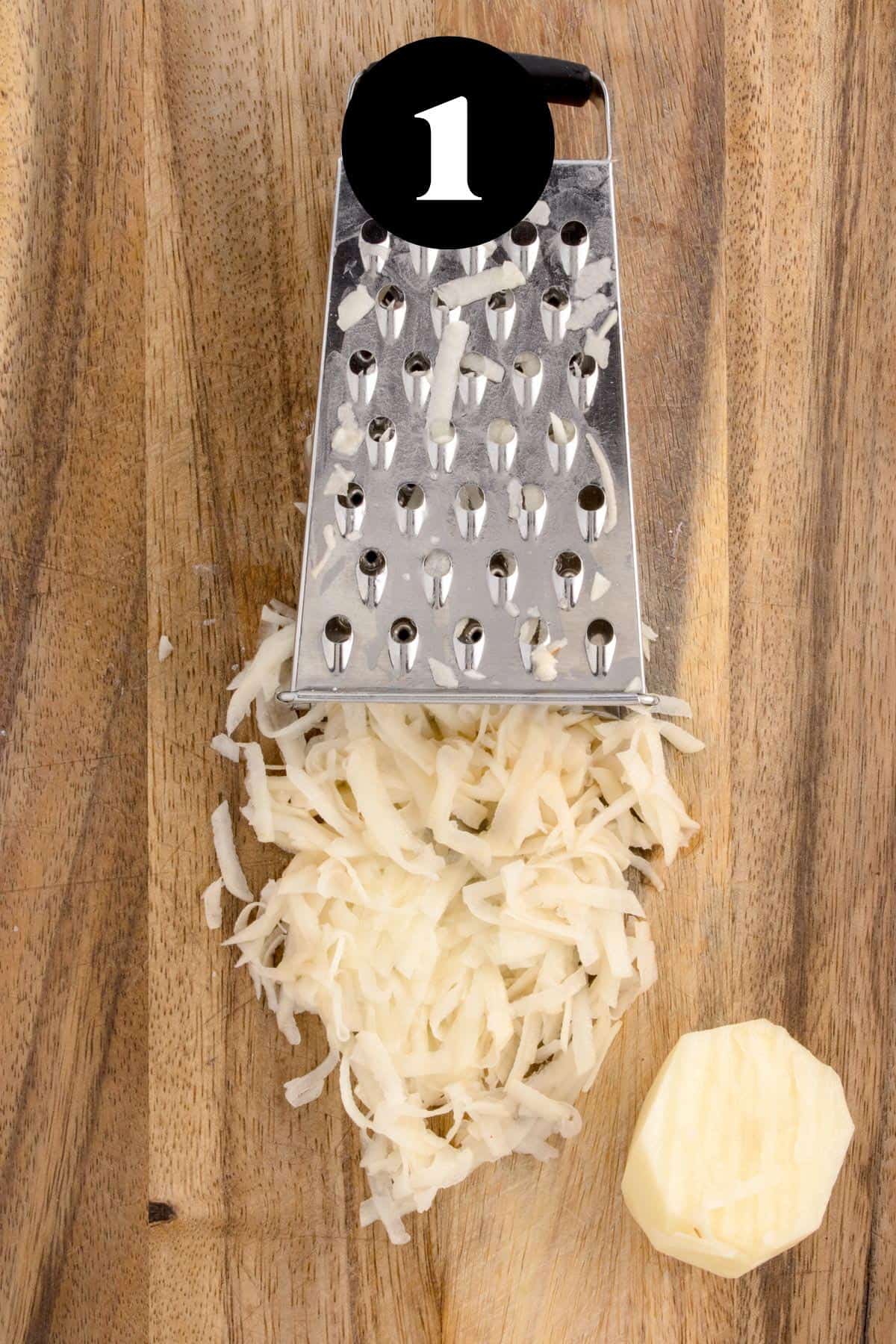 A box grater and some shredded potatoes on a cutting board.