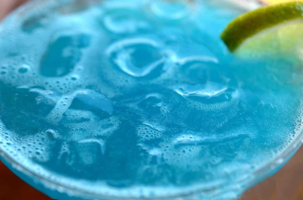A close up of a blue drink with a lime garnish.