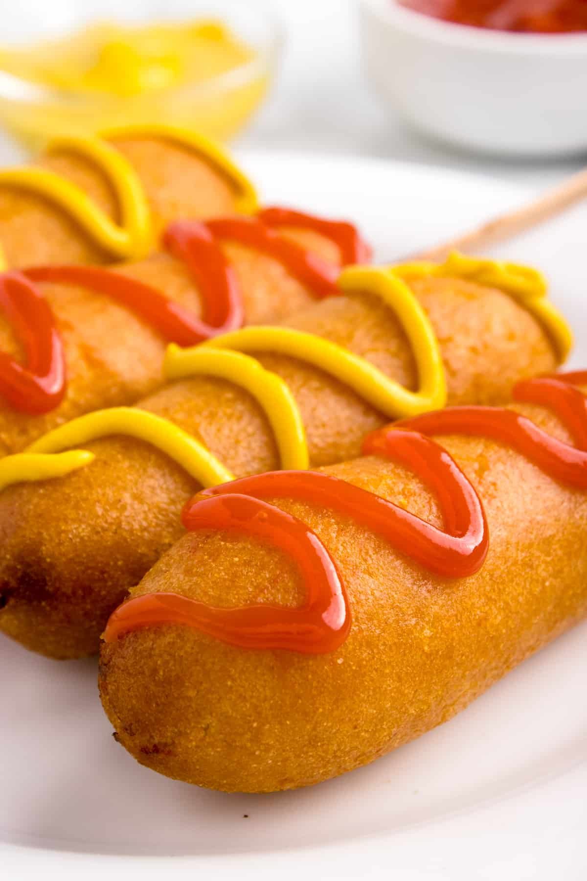 A plate of corn dogs with ketchup and mustard.