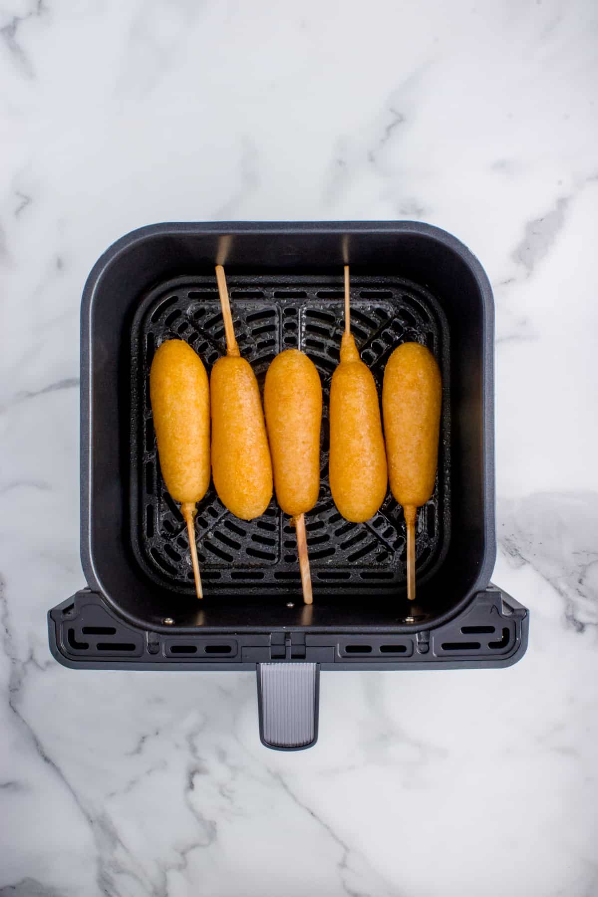 Some corn dogs in an air fryer basket.