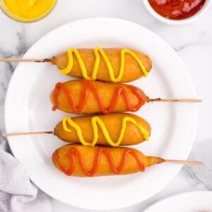 A plate of corn dogs with ketchup and mustard on them.